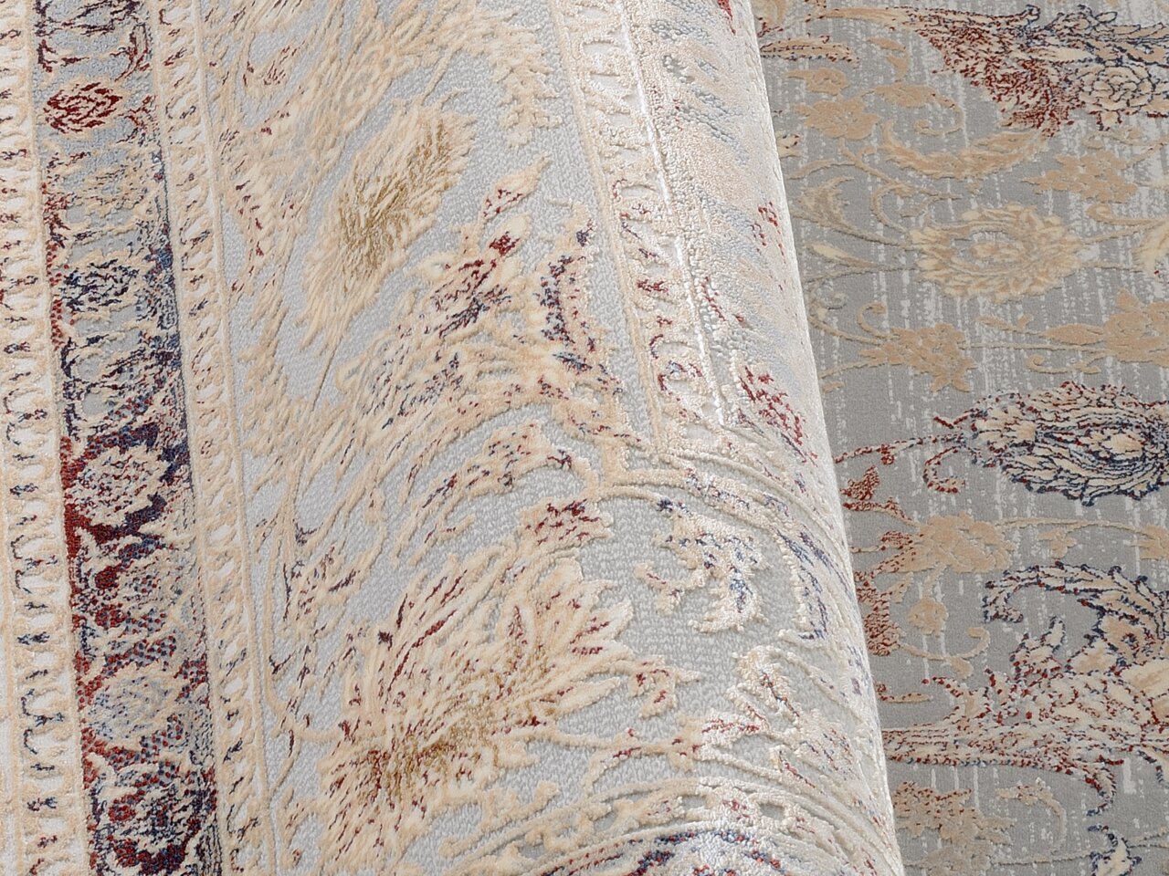 Nahaufnahme eines Orientteppichs mit floralen Mustern in Beige, Blau und Rot, perspektivisch von der Seite aufgenommen.