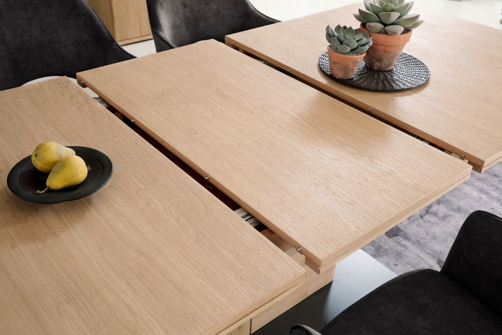 Esstisch aus hellem Holz mit ausziehbarer Funktion, darauf stehen zwei Sukkulenten in Töpfen und eine Schale mit Birnen, Perspektive von oben.