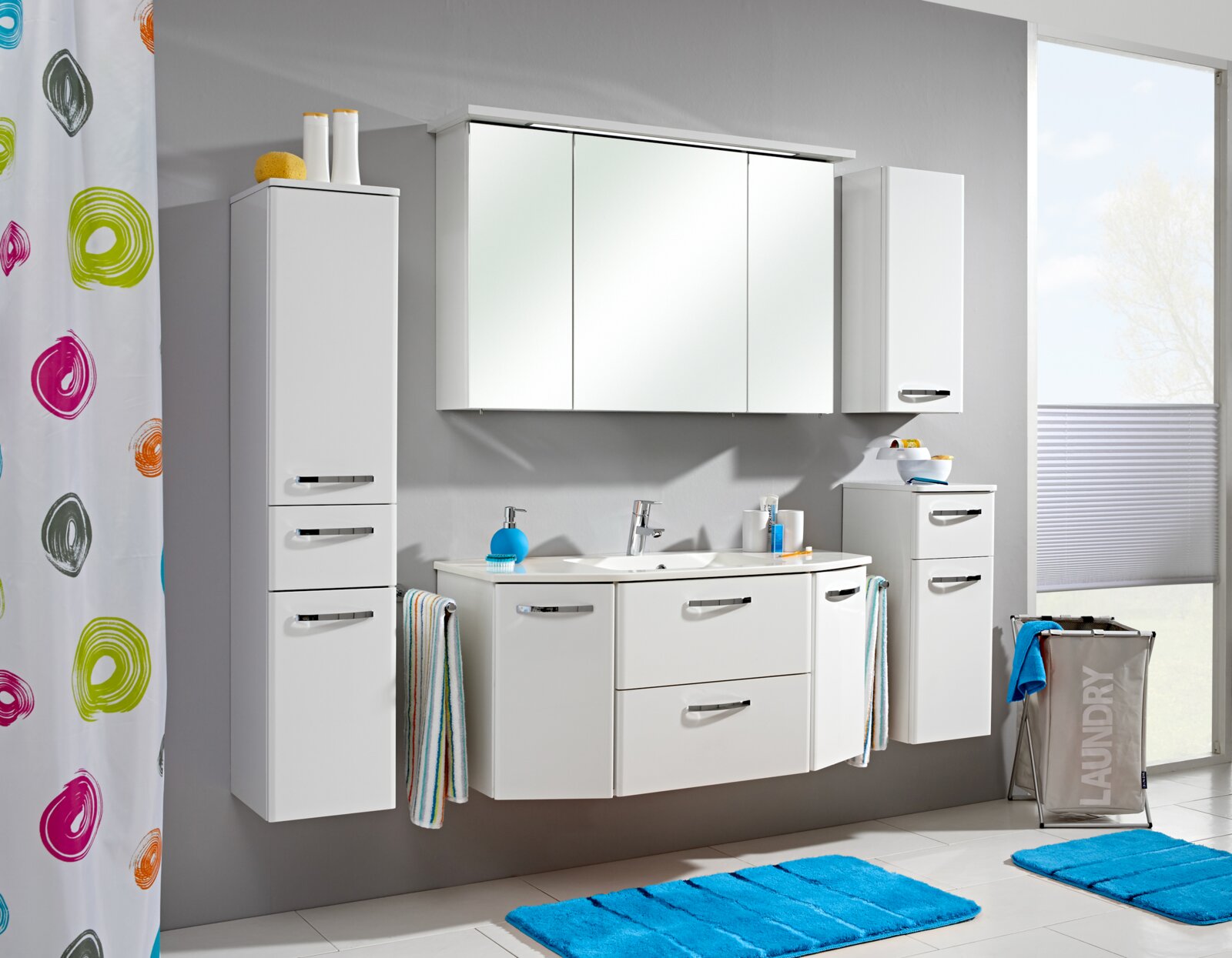 Moderne witte badkamermeubelset met wastafel, onderkast, spiegelkast en twee hoge kasten tegen een grijze muur, gezien van voren.