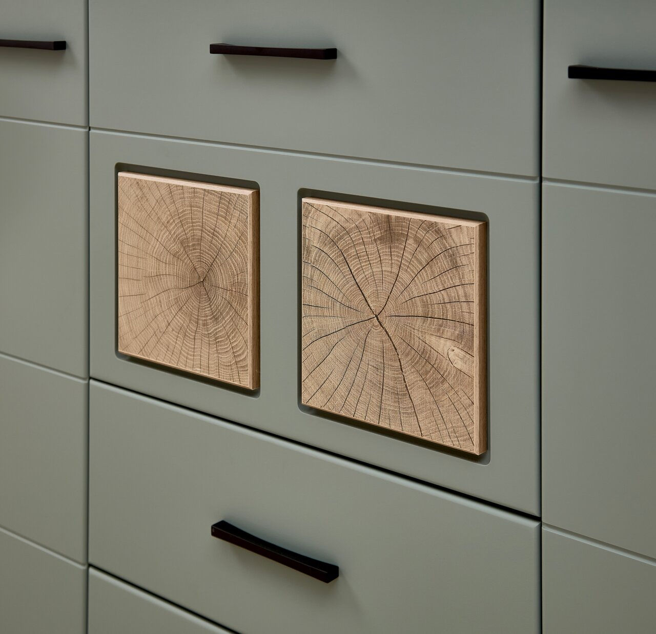 Detailfoto van een wandmeubel met groenachtige lades en decoratieve houten inzetstukken met jaarringen.