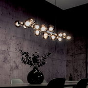 Moderne LED-Pendelleuchte mit mehreren kugelförmigen Leuchten, hängend über einem Esstisch in einem stilvoll eingerichteten Raum, seitliche Perspektive.