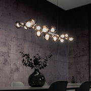 Moderne LED-Pendelleuchte mit mehreren kugelförmigen Leuchten, hängend über einem Esstisch in einem stilvoll eingerichteten Raum, seitliche Perspektive.
