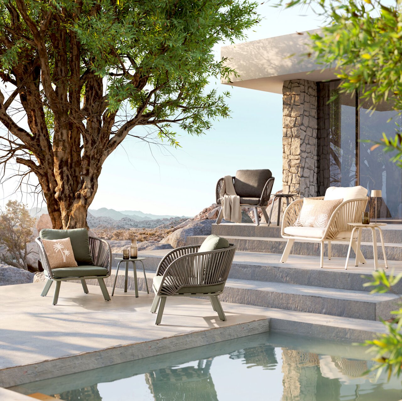 Outdoor-Lounge-Set mit vier modernen Sesseln in Grün, Grau und Beige sowie Beistelltischen auf einer Terrasse am Pool neben einem Haus aus Naturstein, seitliche Perspektive auf die Sitzgruppe