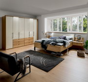 Schlafzimmer mit Dieter Knoll Gleittüren-Funktionsschrank AMATO, Futonbett und Nachtkonsolen in moderner Holzoptik, seitliche Perspektive