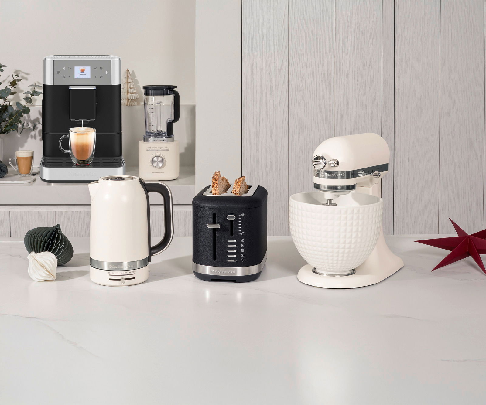 KitchenAid Toaster 2er Monochrome 5KMT2109EPL Schwarzer 2-Scheiben-Toaster mit Brotscheiben, frontal auf einer Küchenarbeitsplatte neben einem Wasserkocher und einer Küchenmaschine platziert.