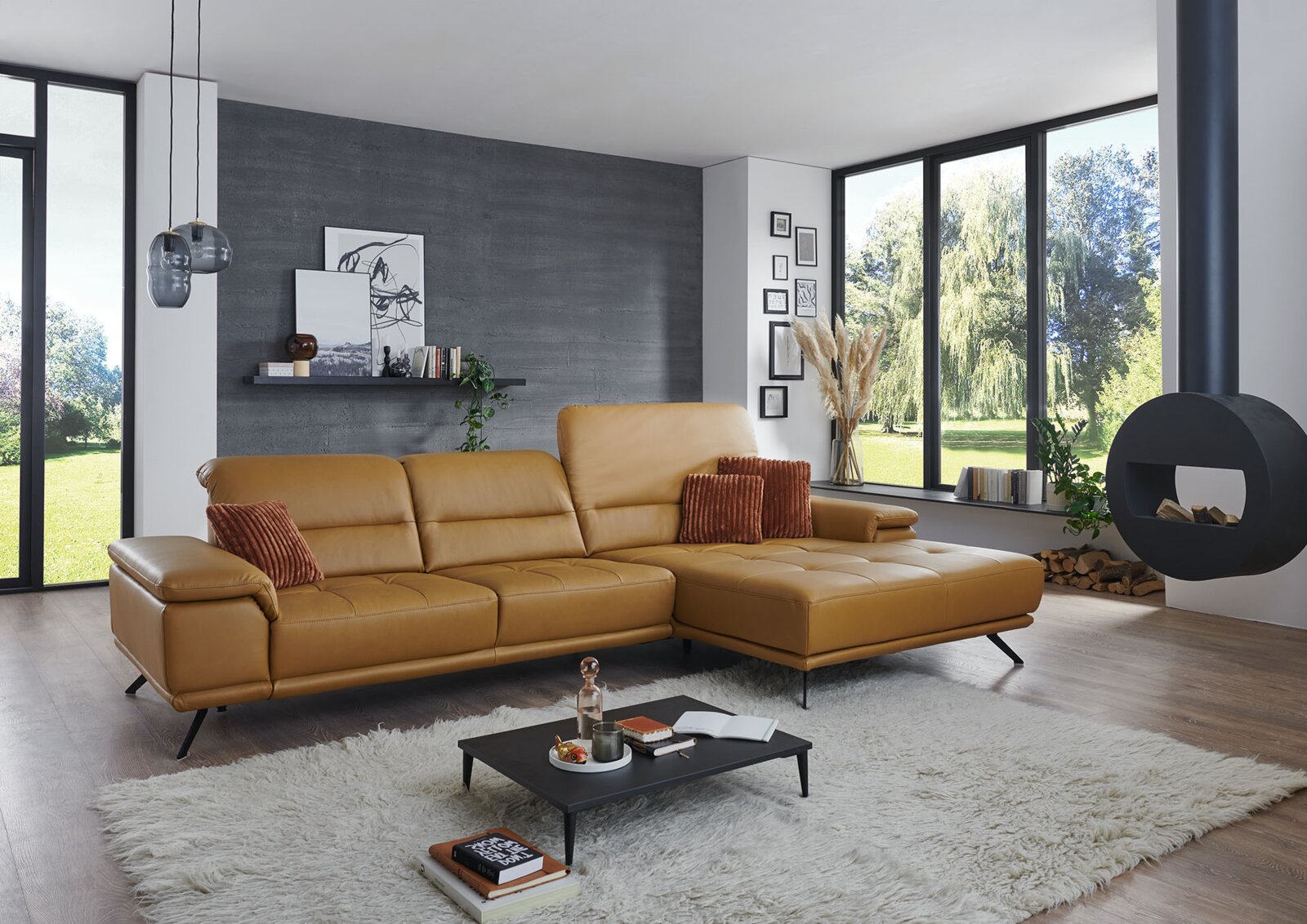 Modernes Wohnzimmersetting mit cognacfarbenem Leder-Ecksofa mit rechter Ottomane/Longchair, gesteppten Sitzflächen und schwarzen Metallfüßen; Perspektive: frontale, leicht seitliche Ansicht von links auf das Sofa.