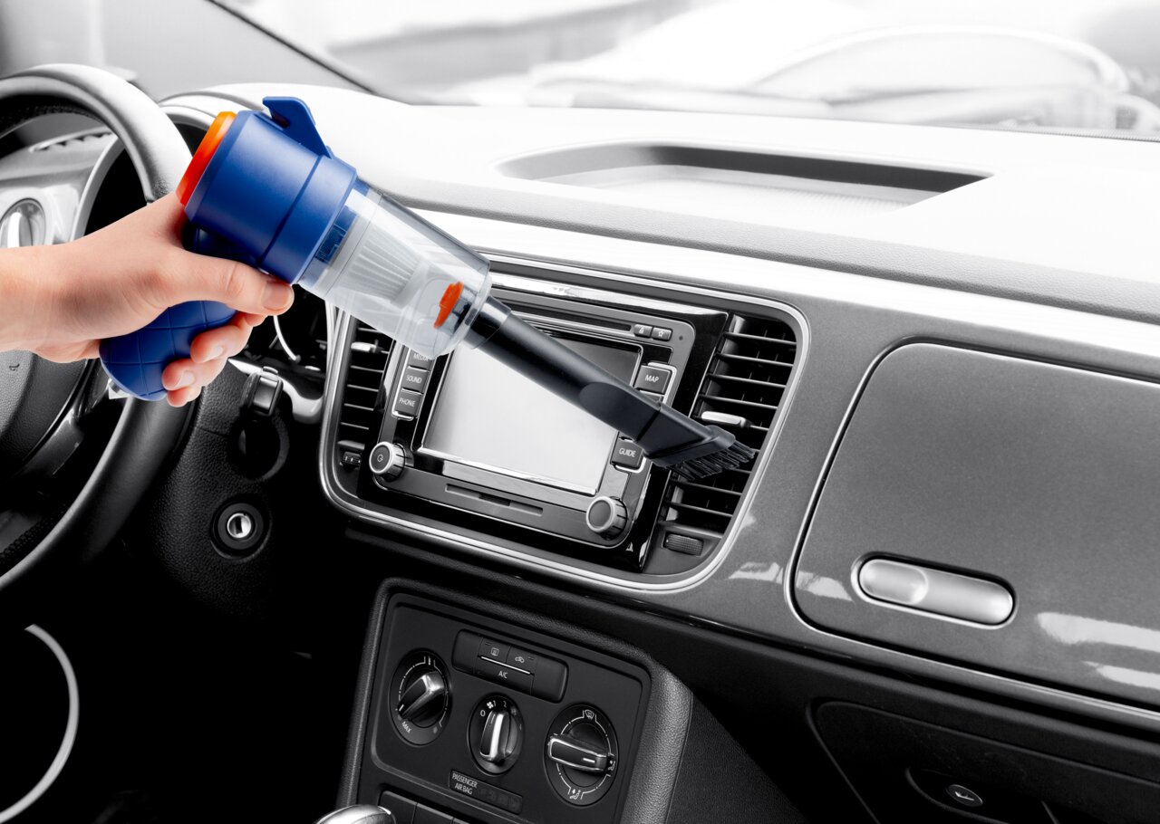 Handstaubsauger in der Hand, der das Armaturenbrett eines Autos aus der Innenperspektive reinigt