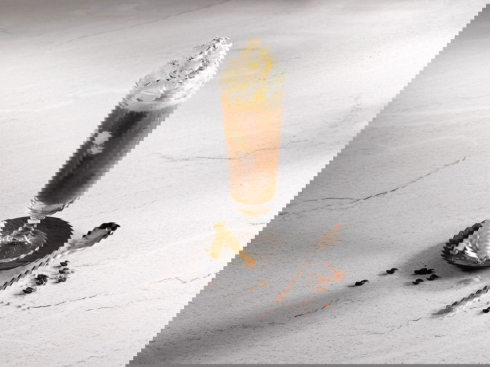 Eiskaffee im Glas mit Sahnehaube, dazu Waffelröllchen und Kaffeebohnen.