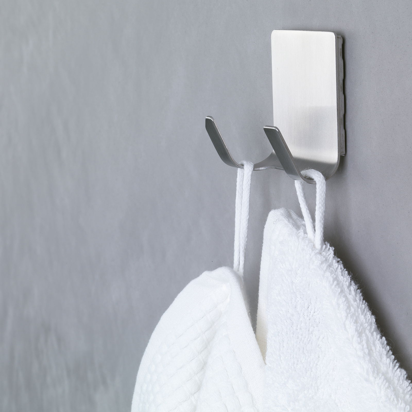 Tesa Powerstrips WATERPROOF Nahaufnahme eines an der Wand befestigten, wasserfesten tesa Powerstrips Hakens mit zwei Handtüchern.