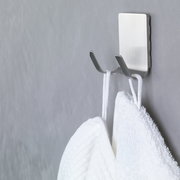 Nahaufnahme eines an der Wand befestigten, wasserfesten tesa Powerstrips Hakens mit zwei Handtüchern.