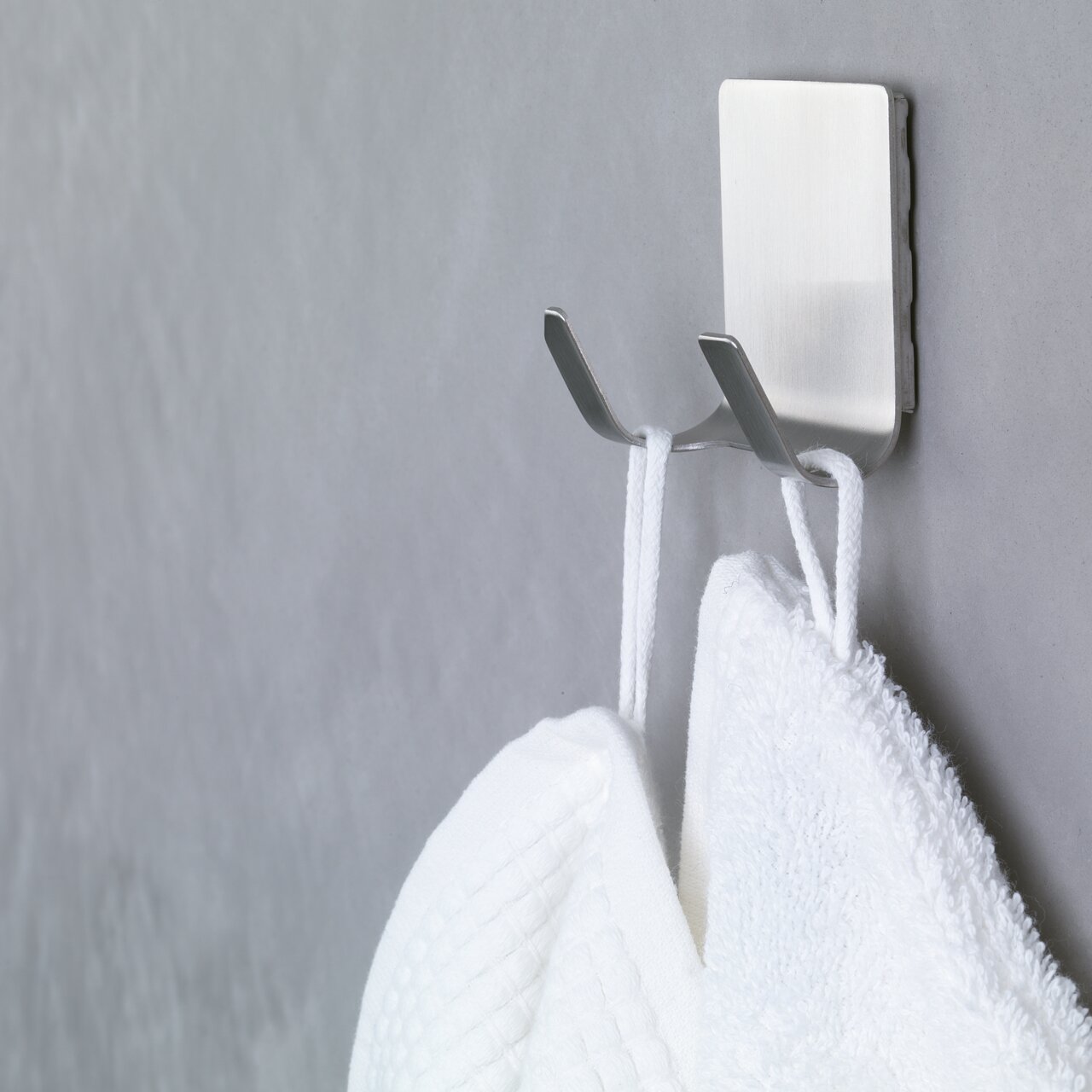 Tesa Powerstrips WATERPROOF Nahaufnahme eines an der Wand befestigten, wasserfesten tesa Powerstrips Hakens mit zwei Handtüchern.