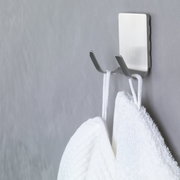 Nahaufnahme eines an der Wand befestigten, wasserfesten tesa Powerstrips Hakens mit zwei Handtüchern.