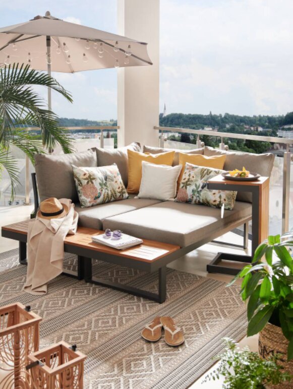 Gartenlounge auf Balkon mit grauen Kissen, Holztisch und Sonnenschirm, seitliche Perspektive