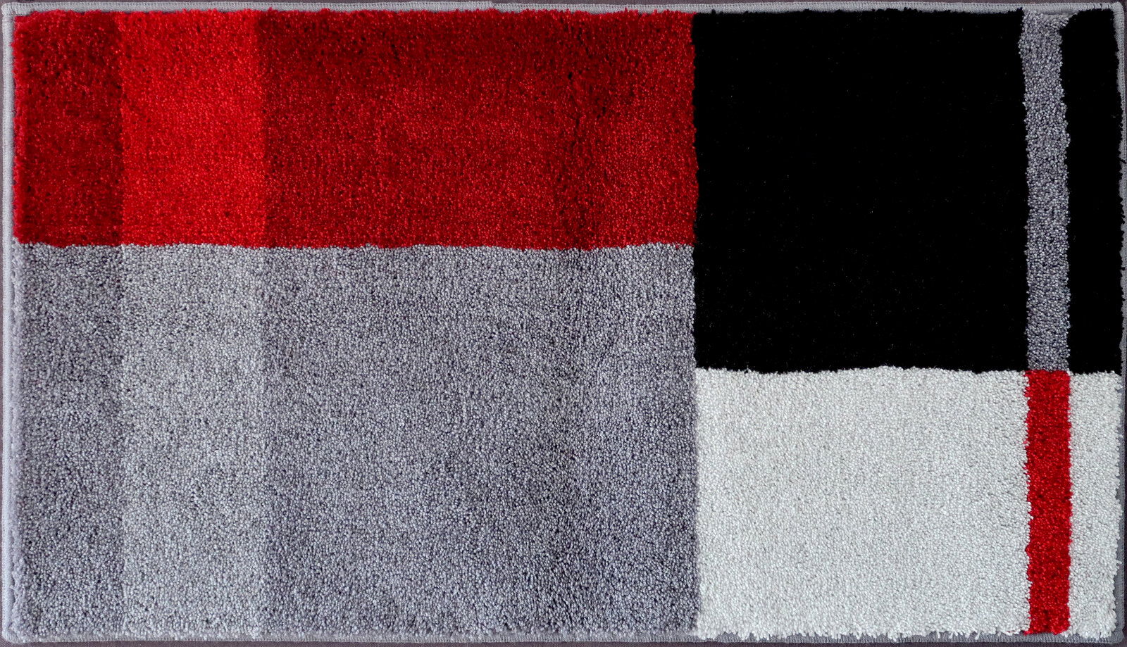Badteppich in rechteckiger Form mit einem modernen geometrischen Muster in Rot, Schwarz, Grau und Weiß, aus der Vogelperspektive fotografiert.