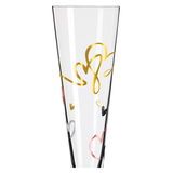 Nahaufnahme eines Champagnerglases mit goldenen und bunten Herzmotiven auf der Oberfläche.
