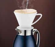 Isolierkanne Venezia in tiefem Blau mit einem weißen Kaffeefilteraufsatz, aus dem heißes Wasser dampft, seitliche Perspektive