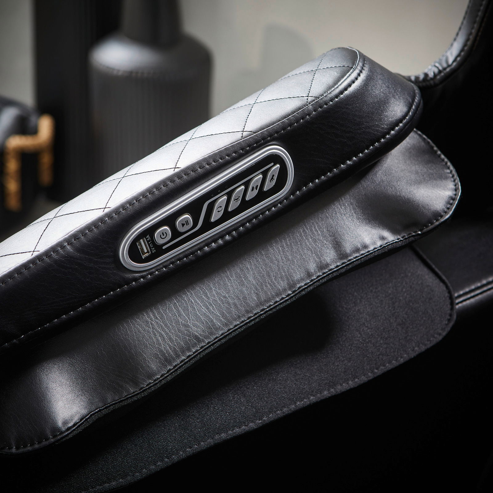 Nahaufnahme eines Massagesessels mit schwarzer Lederpolsterung und integrierter Steuerungseinheit an der Armlehne.