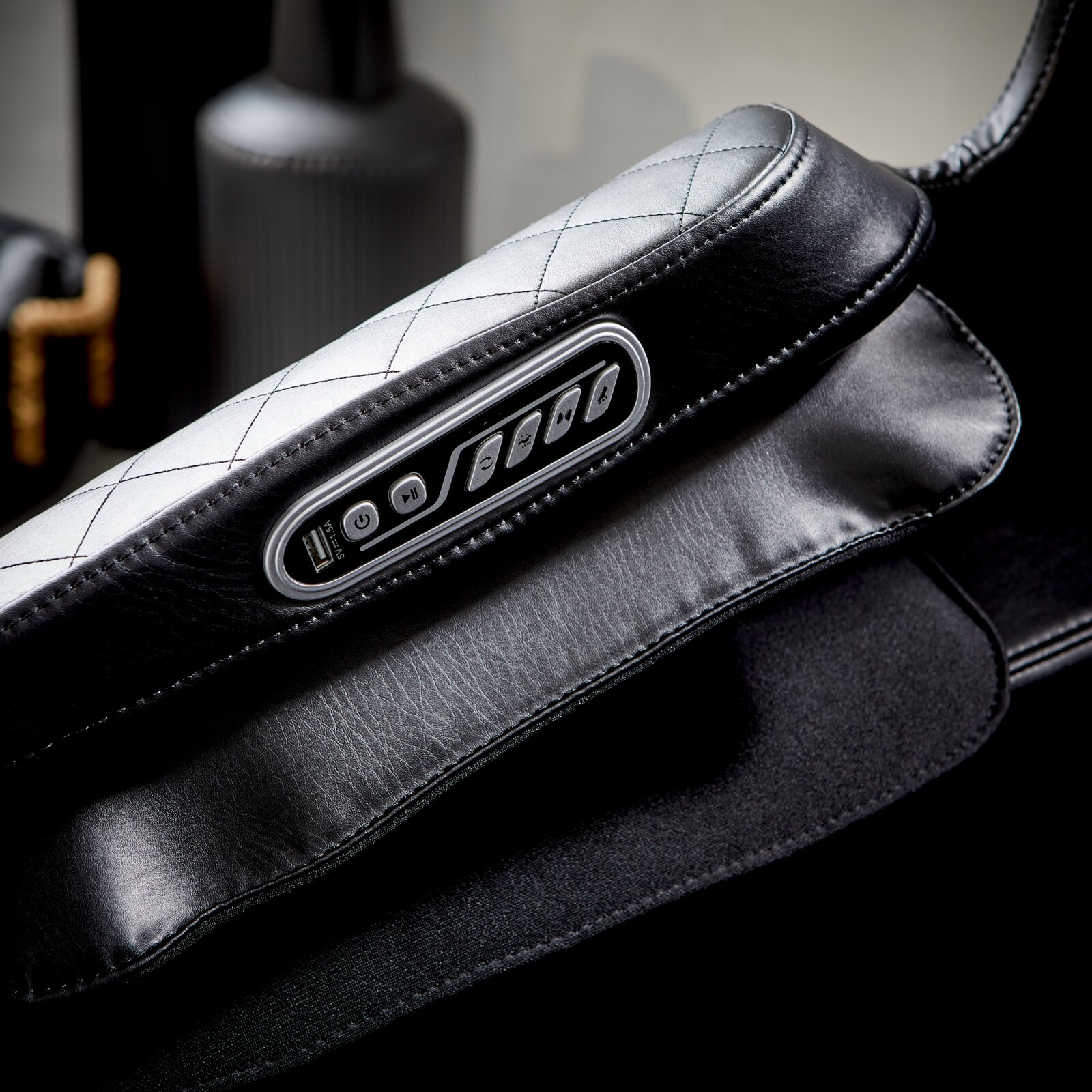 Close-up van een massagestoel met zwarte lederen bekleding en een geïntegreerde bedieningseenheid in de armleuning.