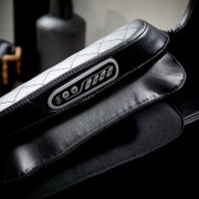 Close-up van een massagestoel met zwarte lederen bekleding en een geïntegreerde bedieningseenheid in de armleuning.