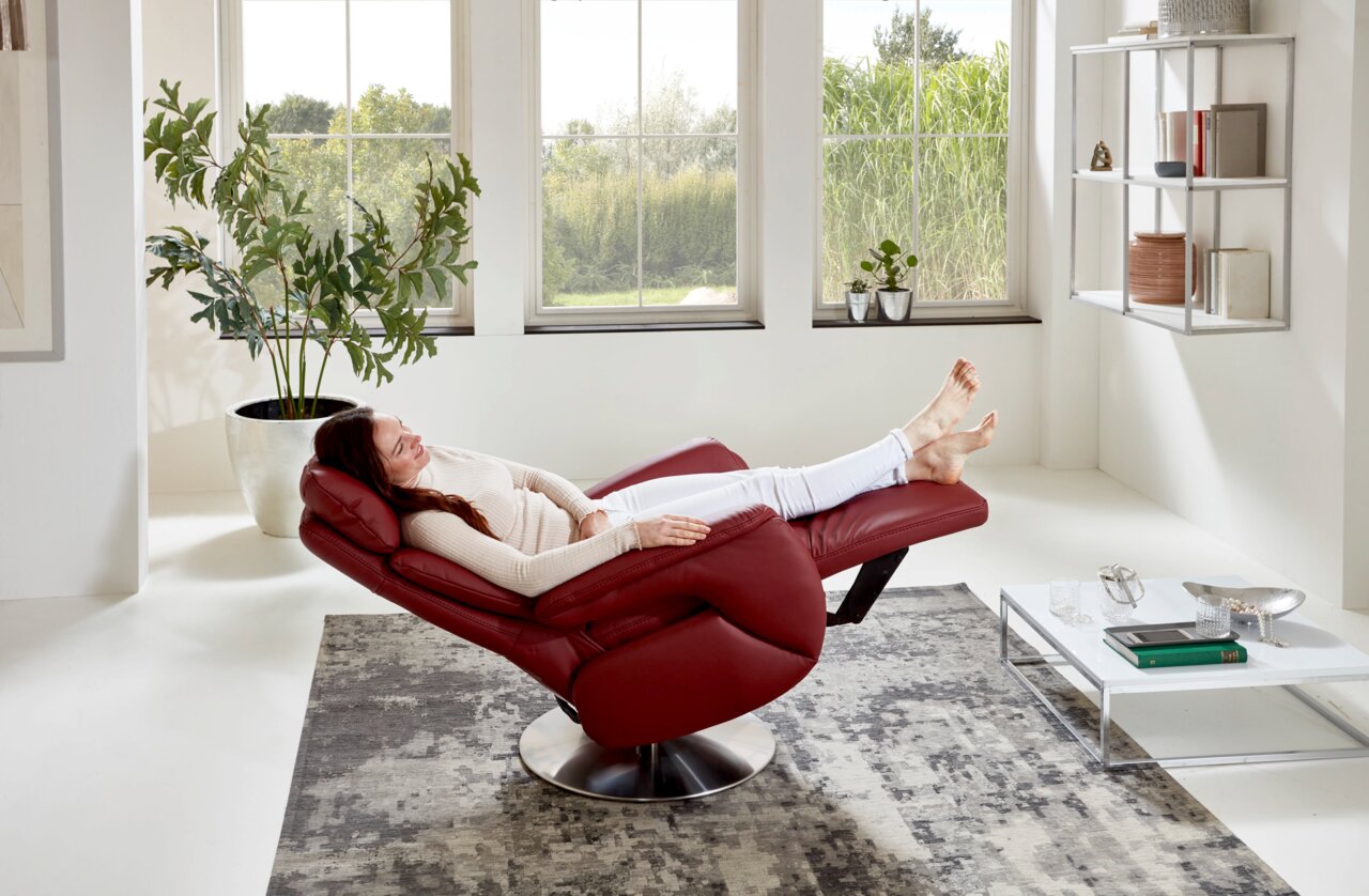 Roter Fernsehsessel in einer modernen Wohnzimmerumgebung, seitliche Perspektive, mit einer Person, die entspannt darauf liegt.