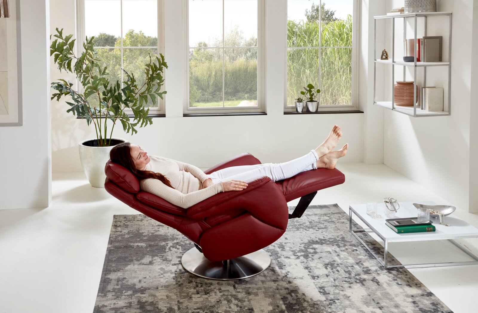 Rode tv-fauteuil in een moderne woonkamer, gezien vanuit de zijkant, met iemand die er ontspannen in ligt.