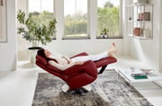 Rode tv-fauteuil in een moderne woonkamer, gezien vanuit de zijkant, met iemand die er ontspannen in ligt.