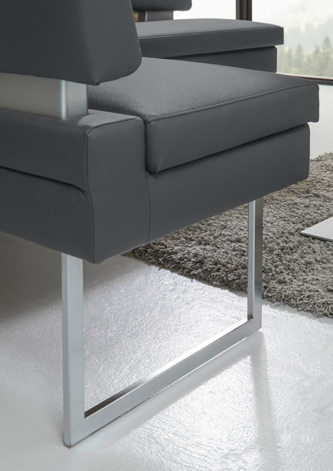 Nahaufnahme einer modernen Eckbank mit grauem Lederbezug und metallenen Kufenbeinen, seitliche Perspektive.