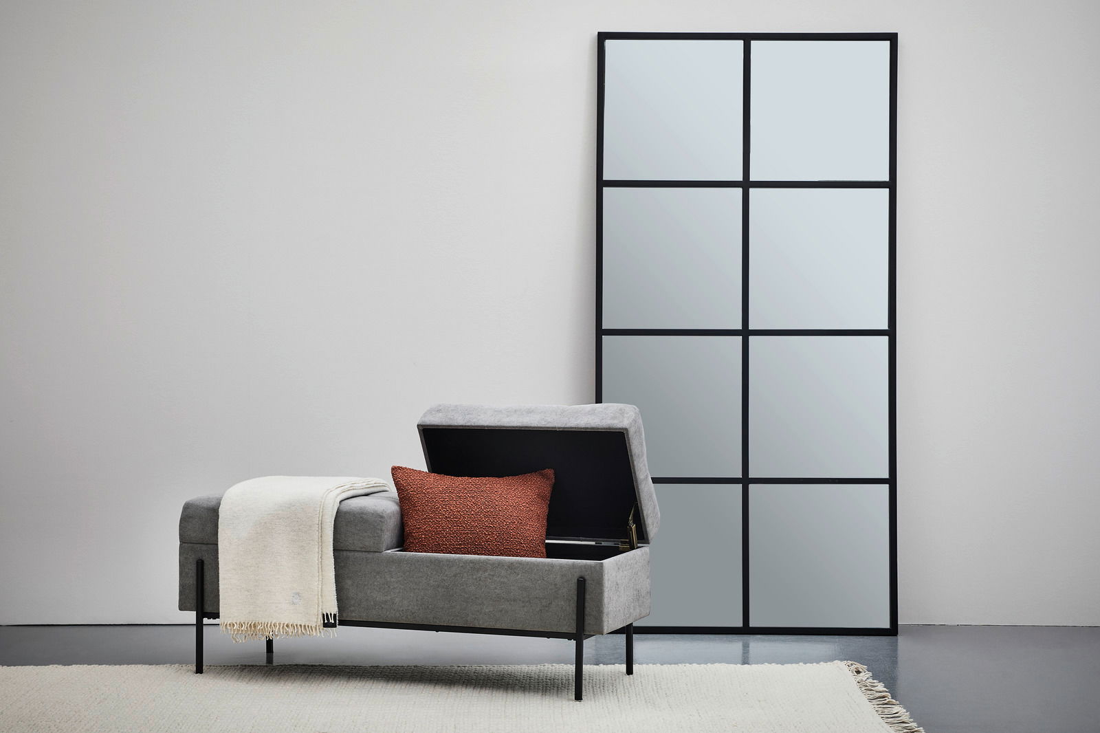 Hockerbank mit Stauraum in grauem Stoff, geöffnet, mit rotem Kissen und weißer Decke, seitliche Perspektive