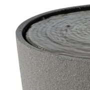 Detailaufnahme eines runden grauen Beton- oder Steinbrunnens mit Wasseroberfläche und kleinen Wellen, Perspektive schräg von oben auf den Rand