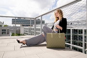 Frau sitzt auf einer Dachterrasse und hält eine olivgrüne Tasche mit Rautenmuster. Die Tasche ist im Vordergrund sichtbar.
