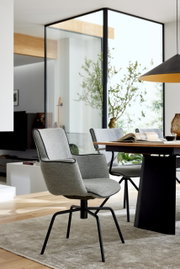 Gestoffeerde eetkamerstoel van lichtgrijze stof met zwarte metalen poten aan een houten tafel in een moderne woonkamer, perspectief: zijaanzicht in driekwart
