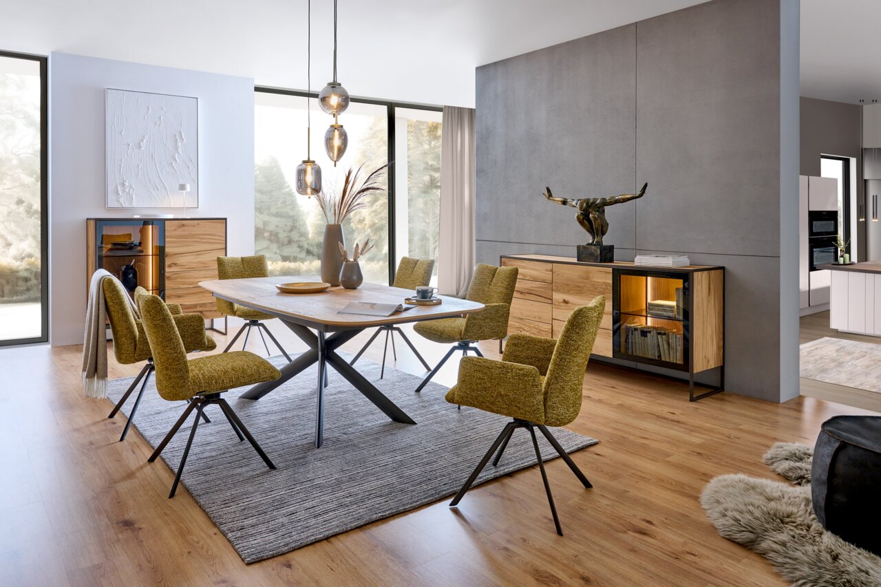 Venjakob Sideboard TAGENA Modernes Esszimmer mit einem eleganten Holztisch und stilvollen Stühlen in einem hellen Raum. Im Hintergrund sind ein Highboard und ein Sideboard aus Holz mit Glasdetails zu sehen. Die Perspektive zeigt den Raum von der Seite, mit Blick auf den Tisch und