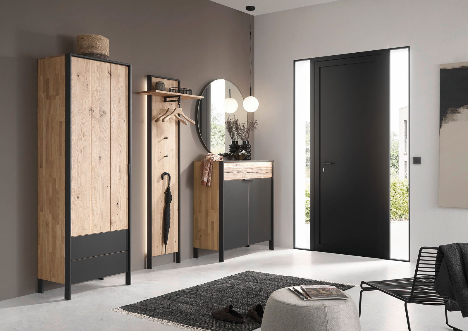 Moderne Garderobeneinrichtung mit Holz- und Metallelementen, bestehend aus einem hohen Schrank, einem Garderobenpaneel mit Haken und einem runden Spiegel, aus der Perspektive des Eingangsbereichs betrachtet.