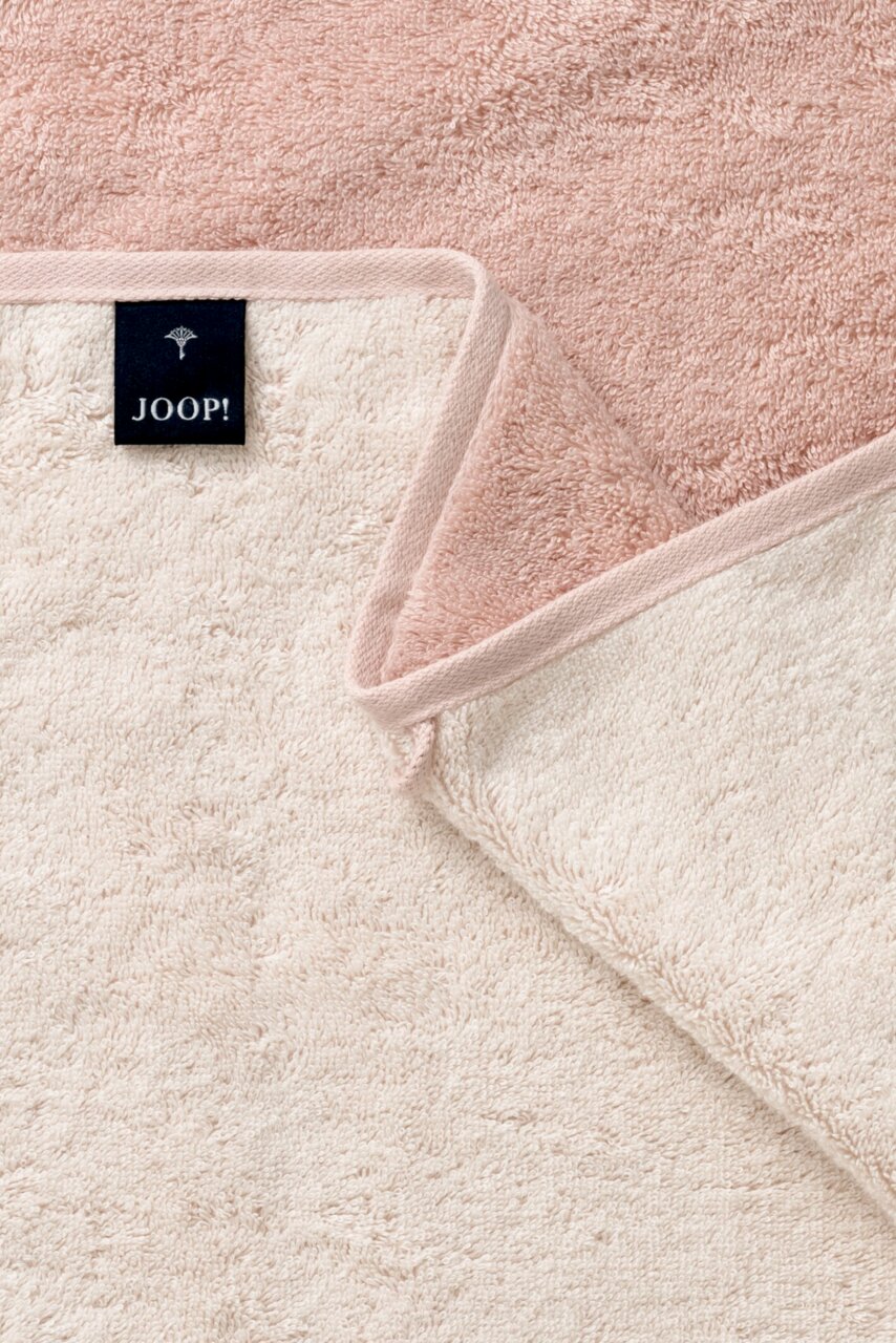 Nahaufnahme eines zweifarbigen Handtuchs in Rosa und Creme mit einem Joop-Label, das die weiche Textur und die Kanten zeigt.