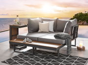 Gartenlounge mit grauen Kissen und Holzdetails, seitliche Perspektive, im Hintergrund Sonnenuntergang über dem Meer