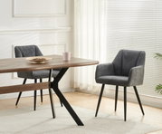 Schwarzer Esstisch mit Holzplatte und X-förmigem Metallgestell, daneben zwei graue Polsterstühle im hellen Esszimmer; Perspektive: seitliche 3/4-Ansicht auf Tisch und Stühle.