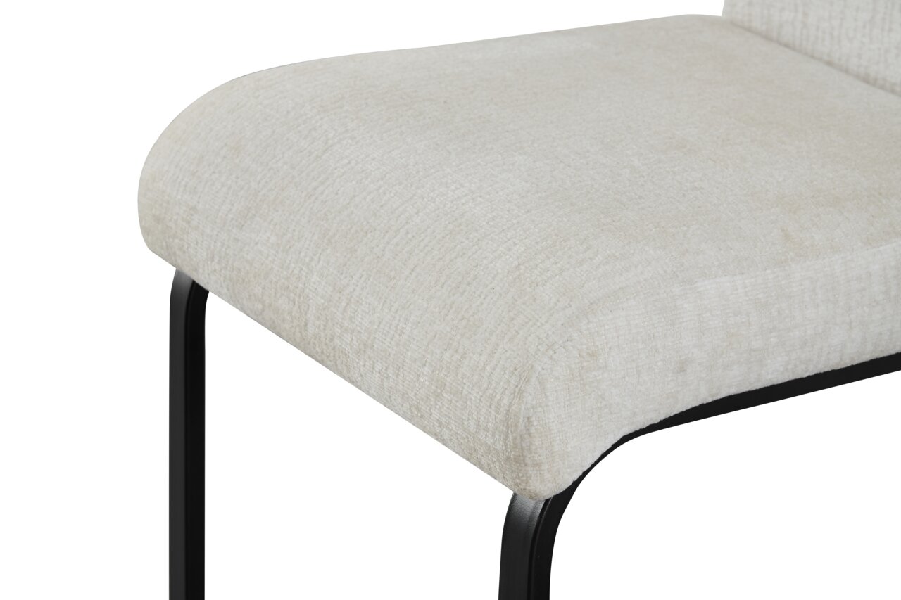 Nahaufnahme eines gepolsterten Sitzkissens in hellem Beige mit schwarzem Metallgestell, schräg von vorne/oben fotografiert