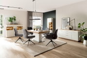 Moderne eetkamerset met een lichte houten tafel, gestoffeerde draaistoelen, witte dressoirs en een vitrinekast met verlichting, evenals een zwarte hanglamp, gefotografeerd vanuit een breedhoekperspectief op ooghoogte.