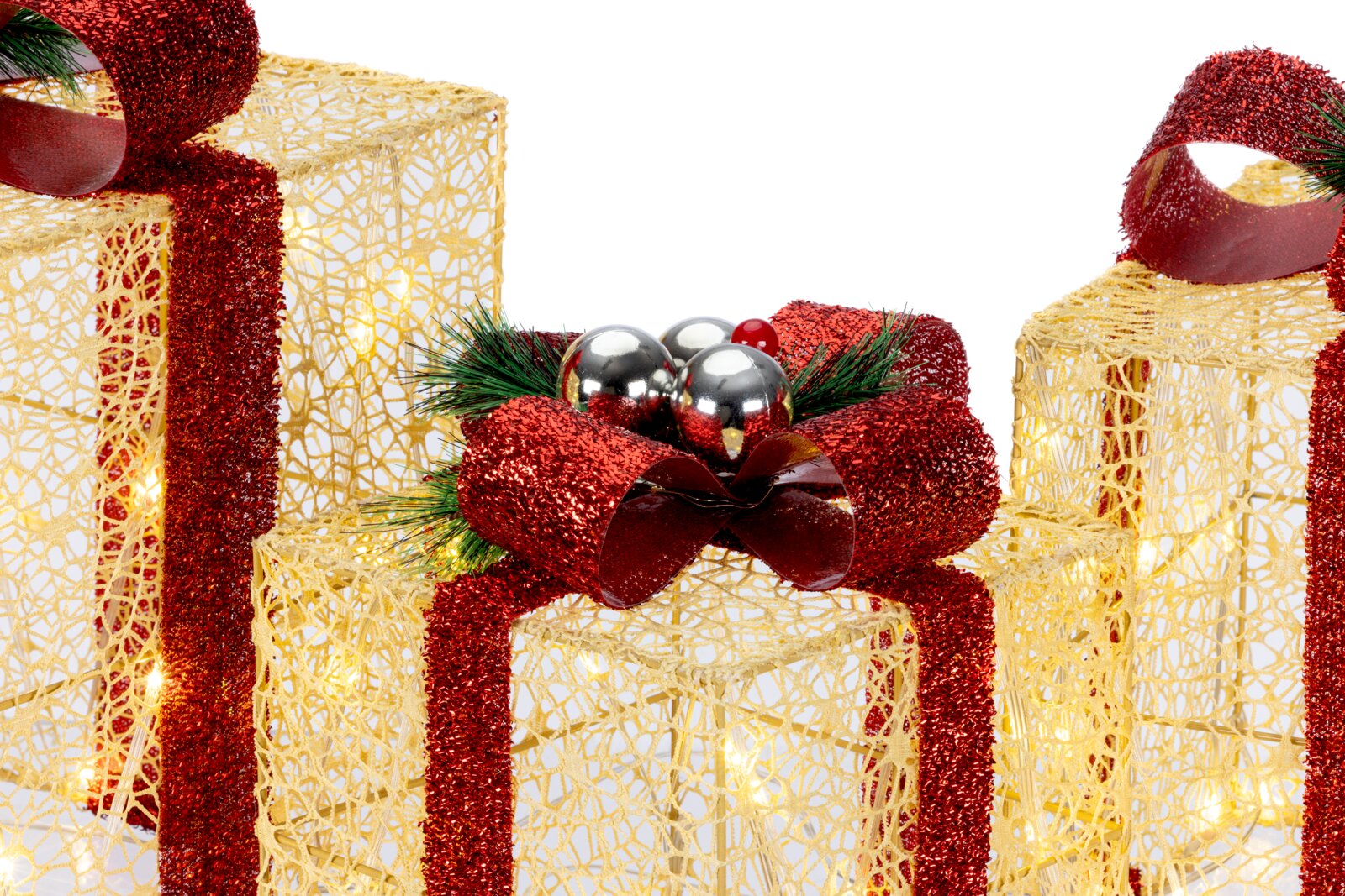 Nahaufnahme in leichter Aufsicht: dekorative Weihnachtsgeschenkboxen aus goldenem Drahtgeflecht mit warmweißer LED-Beleuchtung und roten Glitzer-Schleifen, in der Mitte eine große rote Schleife mit silbernen Kugeln und Tannengrün vor weißem Hintergrund