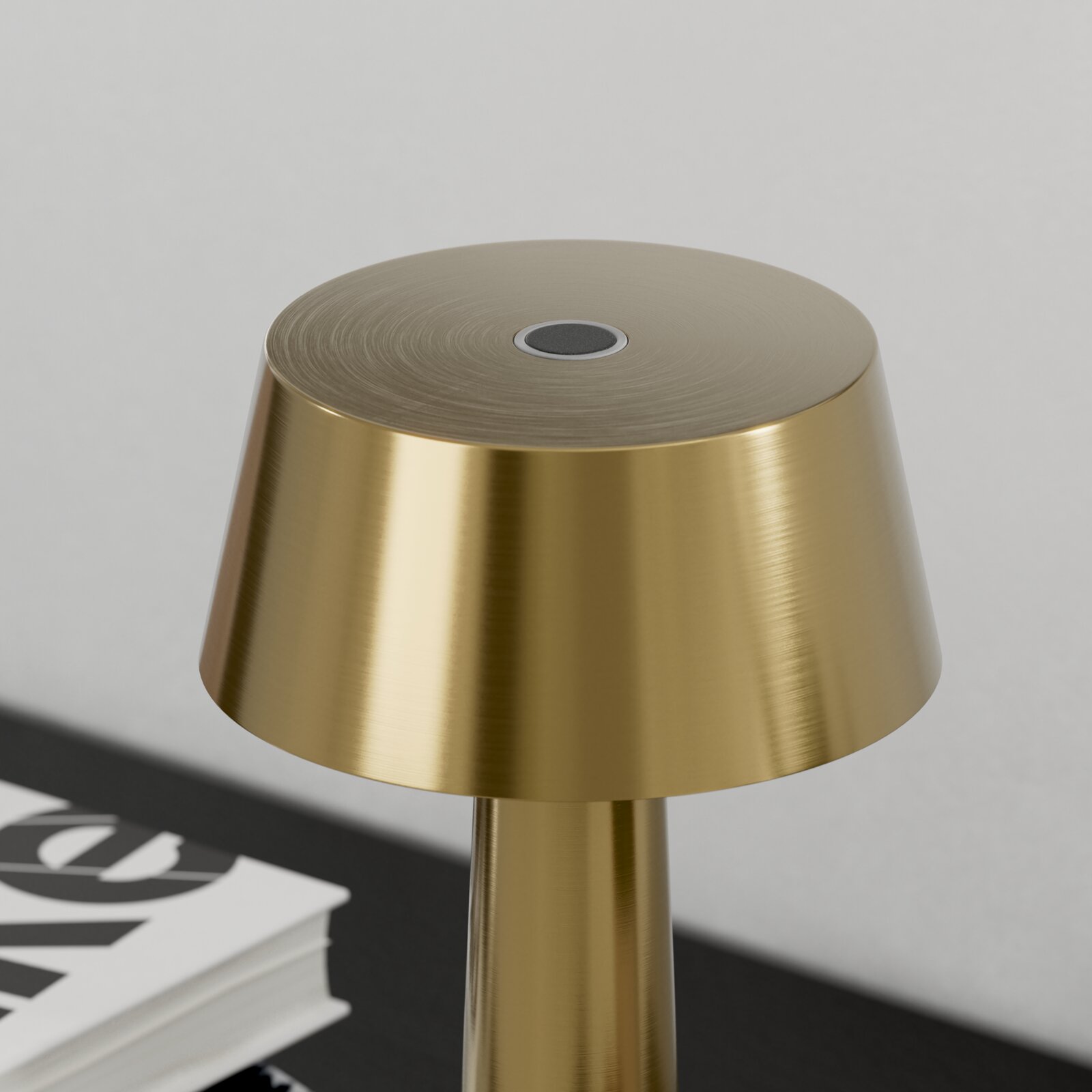 Close-up van een moderne tafellamp van geborsteld messing met een platte, ronde lampenkap en een touchknop in het midden, licht van bovenaf gefotografeerd