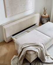 Querschläfer-Sofa mit Hubbeschlag in beiger Farbe, von oben fotografiert, mit einer gestreiften Decke darauf.