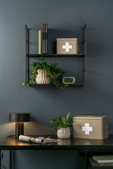 Aufbewahrungsbox MEDICINE in beige mit weißem Kreuz, auf einem Regal und Tisch in einem stilvollen Raum, seitliche Perspektive
