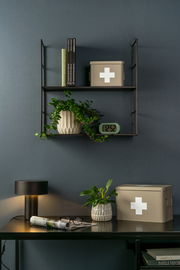 Aufbewahrungsbox MEDICINE in beige mit weißem Kreuz, auf einem Regal und Tisch in einem stilvollen Raum, seitliche Perspektive