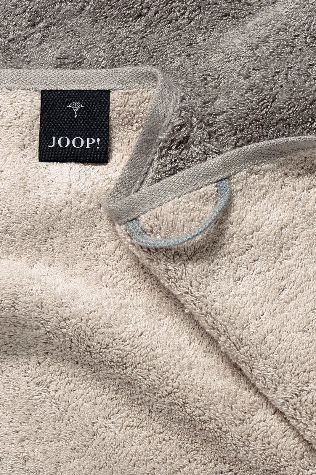 JOOP! Handtuch DOUBLEFACE CLASSIC Nahaufnahme eines beigen Handtuchs mit grauem Rand und einem schwarzen Etikett mit der Aufschrift 'JOOP!'