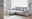 Graues Ecksofa mit Ottomane links, dekoriert mit Kissen und Decke, in einem hellen Wohnzimmer mit Holzboden und Stehlampe, seitliche Perspektive.