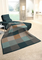 Gemütliche Wohndecke in einem modernen Wohnzimmer, ausgebreitet auf einer Couch, mit einem karierten Muster in Erdtönen und Blick auf einen hellen Raum mit großen Fenstern.