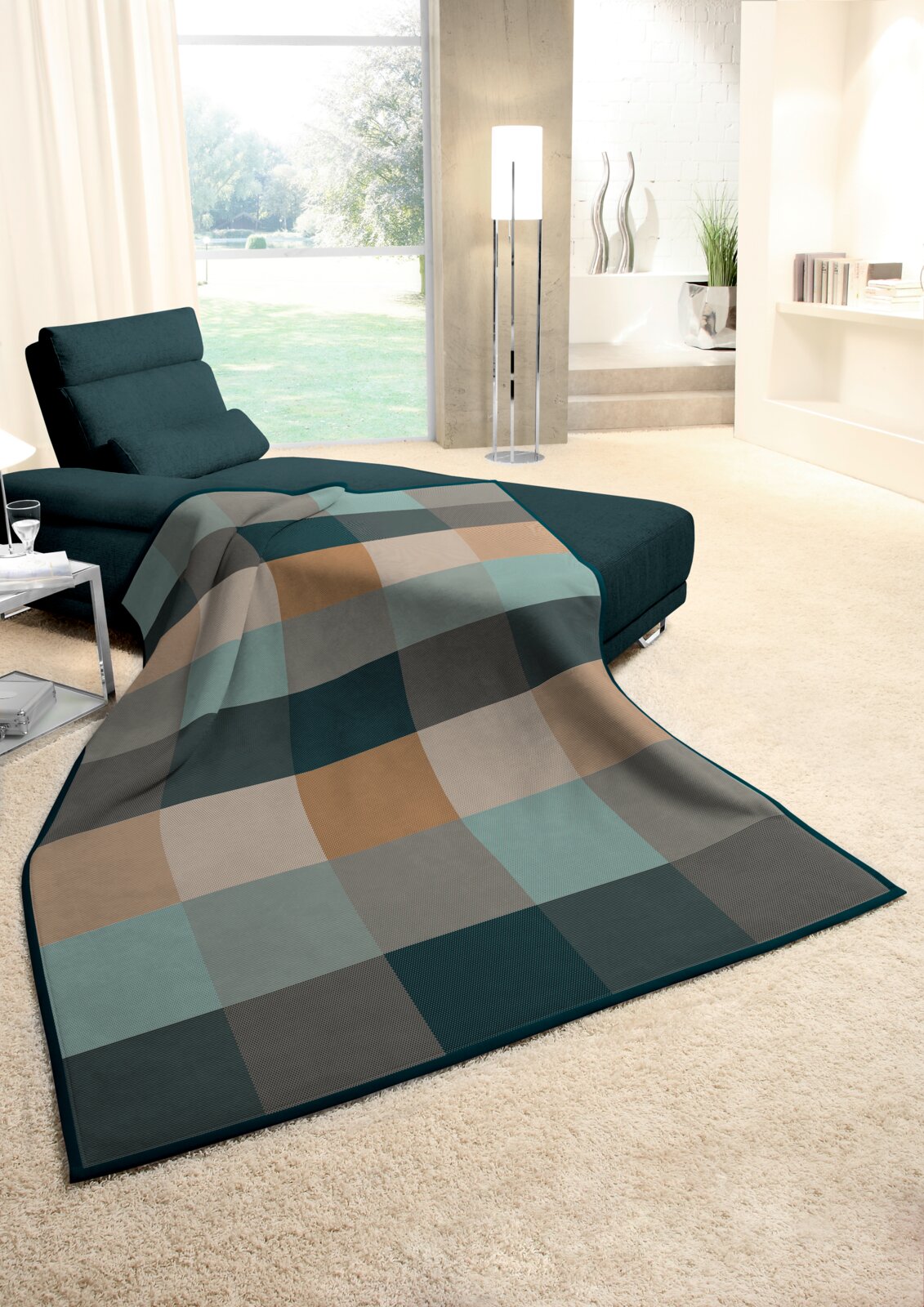 Gemütliche Wohndecke in einem modernen Wohnzimmer, ausgebreitet auf einer Couch, mit einem karierten Muster in Erdtönen und Blick auf einen hellen Raum mit großen Fenstern.