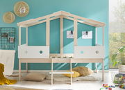 Spielbett in Hausform aus hellem Holz mit weißen Seitenteilen, umgeben von kindgerechter Dekoration, aus der Frontalperspektive.