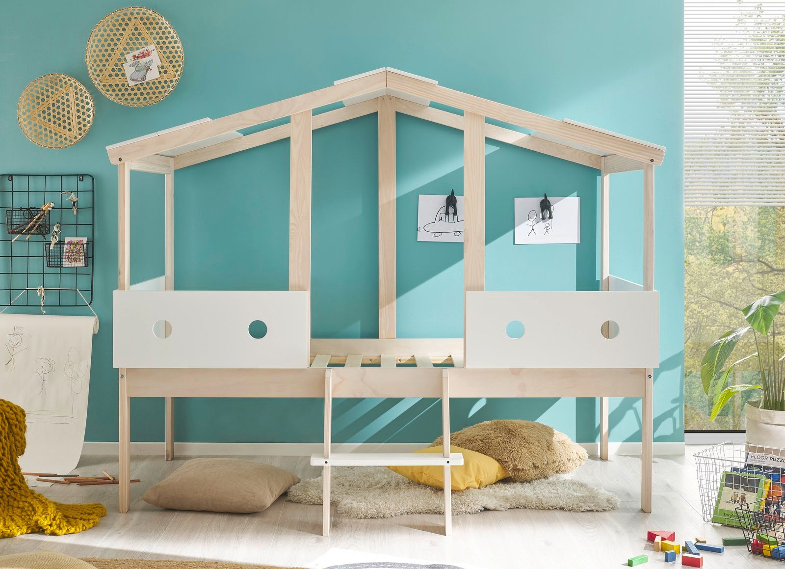 Spielbett in Hausform aus hellem Holz mit weißen Seitenteilen, umgeben von kindgerechter Dekoration, aus der Frontalperspektive.