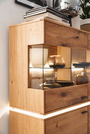 Nahaufnahme eines Highboards aus Holz mit Glaseinsätzen, dekoriert mit Büchern und Geschirr, seitliche Perspektive.